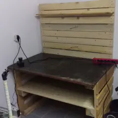 Drewniany stół warsztatowy z półkami, narzędziami i listwą zasilającą.